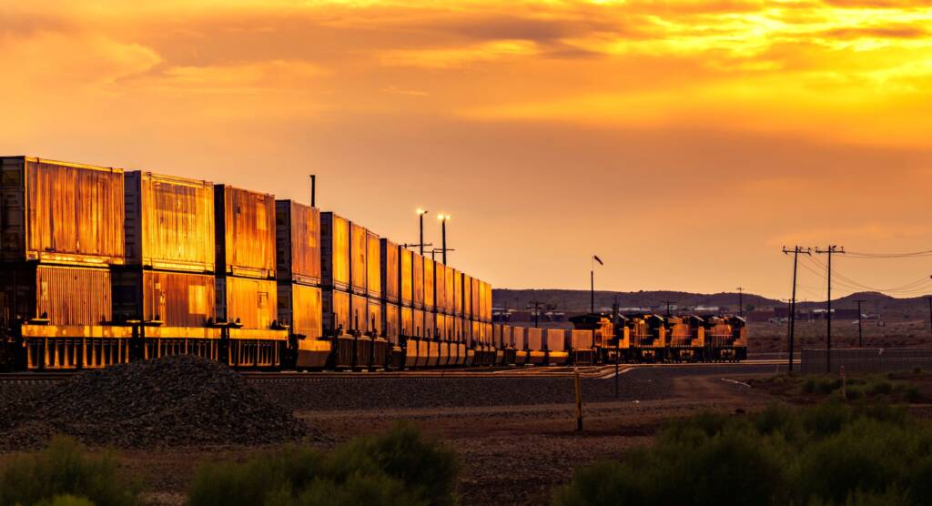 Cargo train on the railroad during bright yellow sunset in the countryside